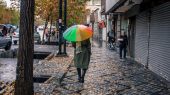 عکسی از هوای بارانی و شخصی که با چتر رنگارنگ در خیابان درحال قدم زدن است